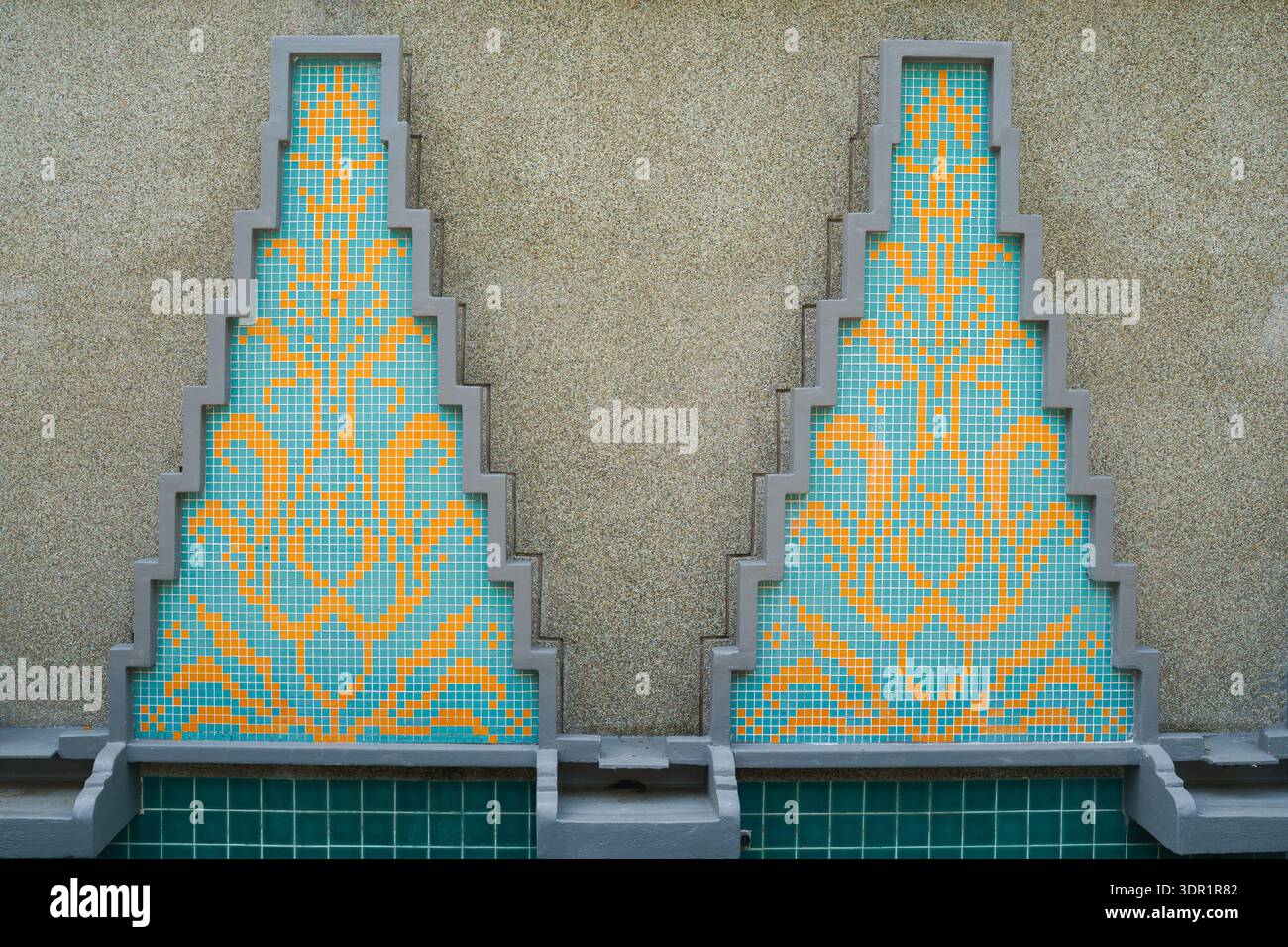 Symmetrical stepped triangular mosaic panels featuring blue and yellow geometric tile patterns on textured wall. Stock Photo