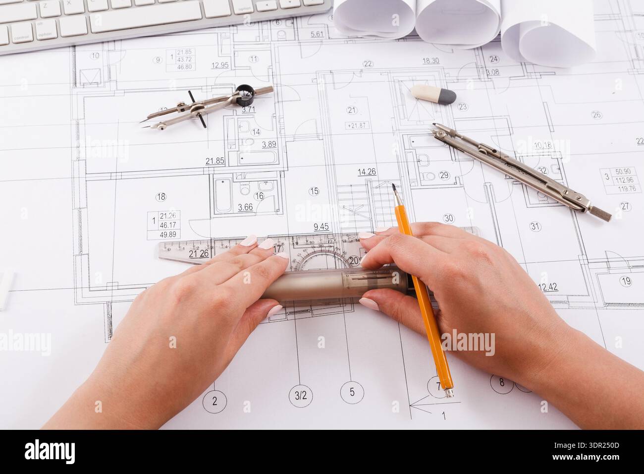 Hands Working on a Design Layout With Tools and Keyboard on a Table in an Office Setting Stock Photo