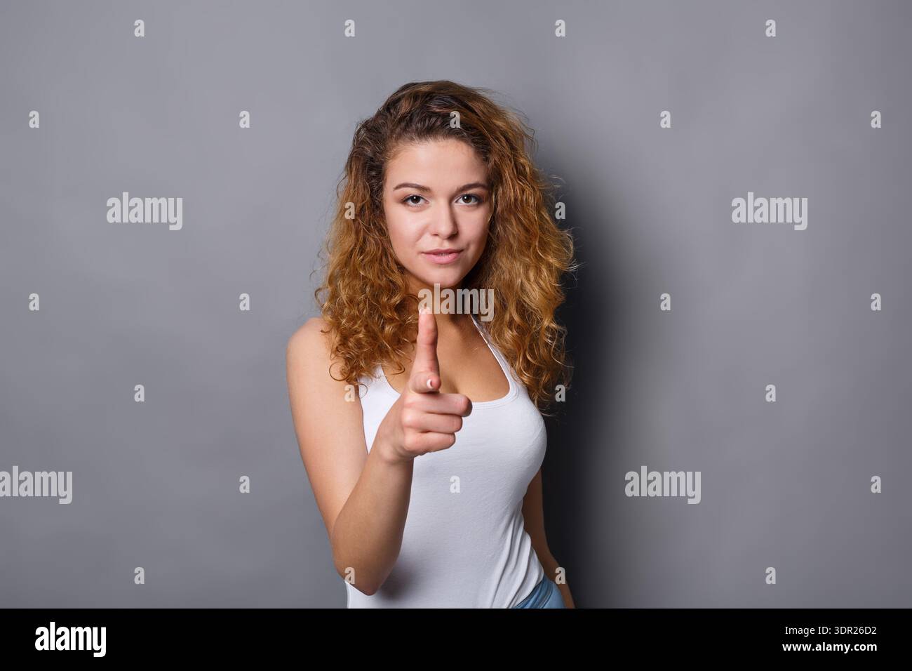 Woman Points Finger While Standing Against a Gray Wall in a Simple Setting Stock Photo