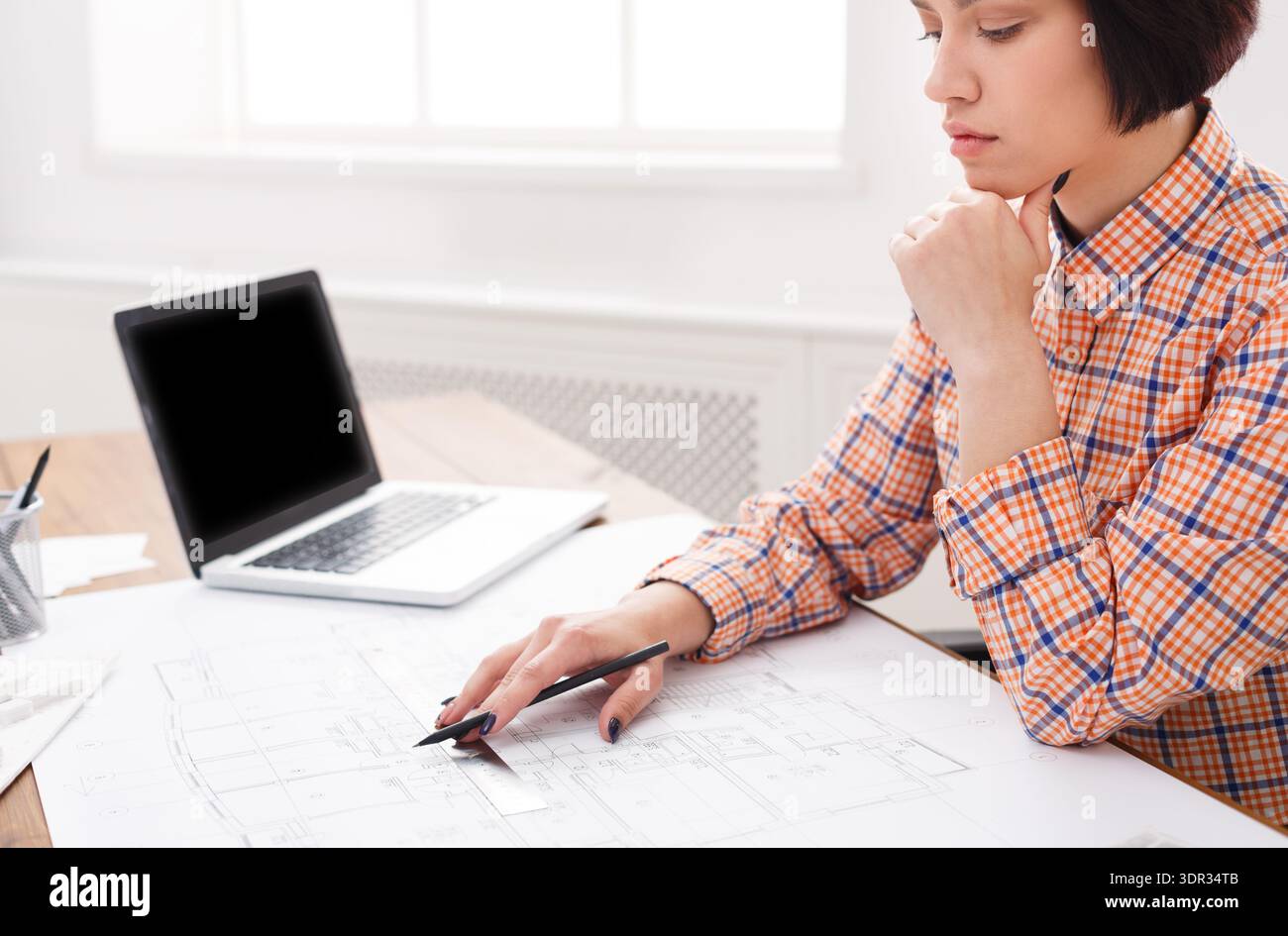 Woman Focuses on Drawing Plans at a Desk in a Bright Office Setting in the Morning Stock Photo