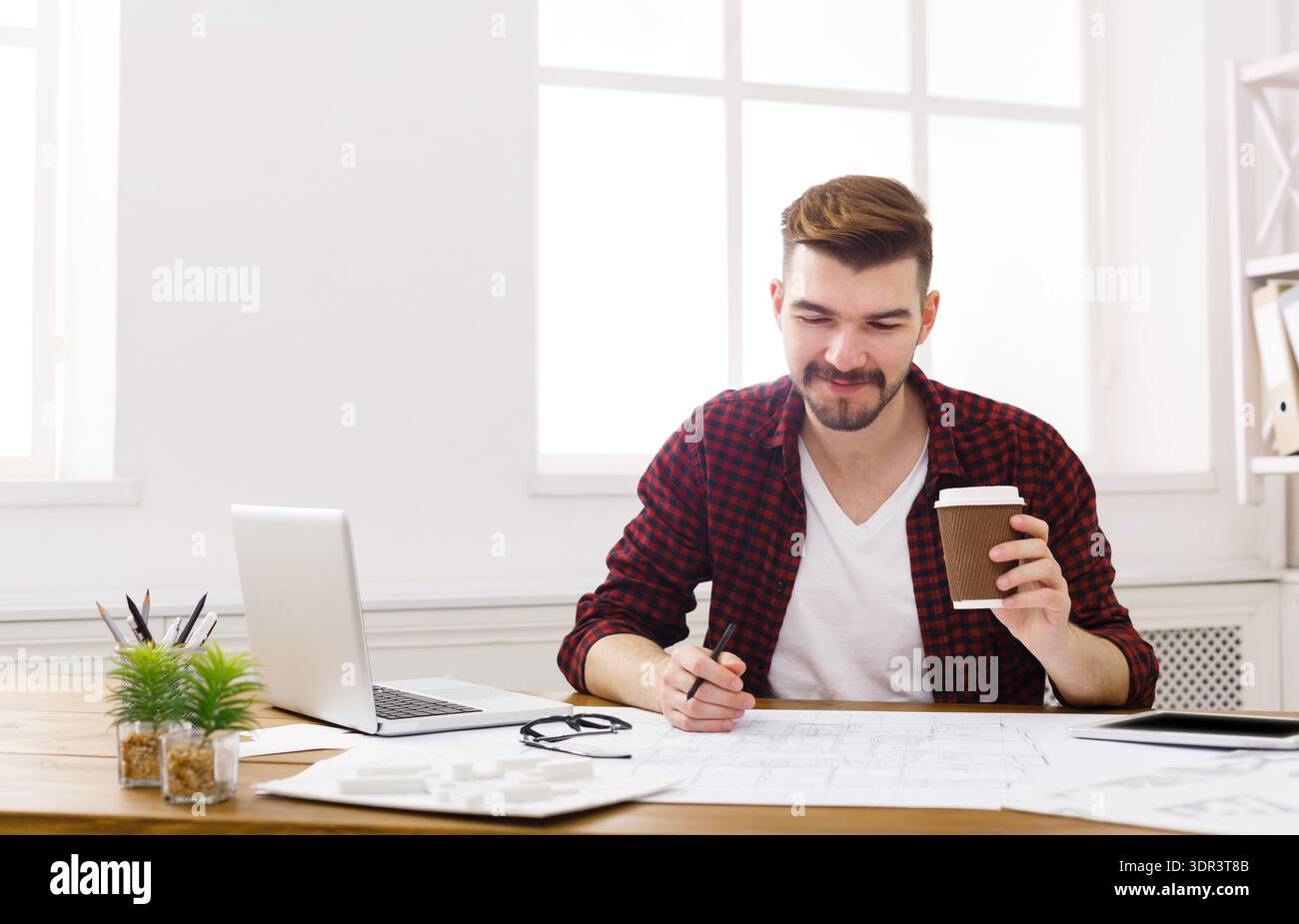 Man Sitting at Desk Working With Laptop and Coffee While Looking at Documents Stock Photo