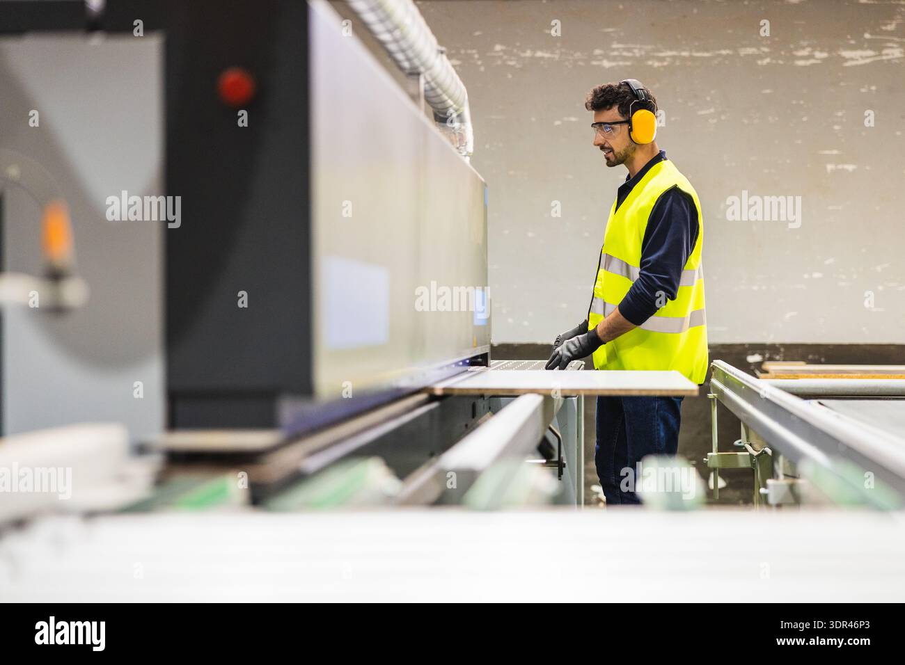 Worker operating industrial cutting machine in lumberyard Stock Photo