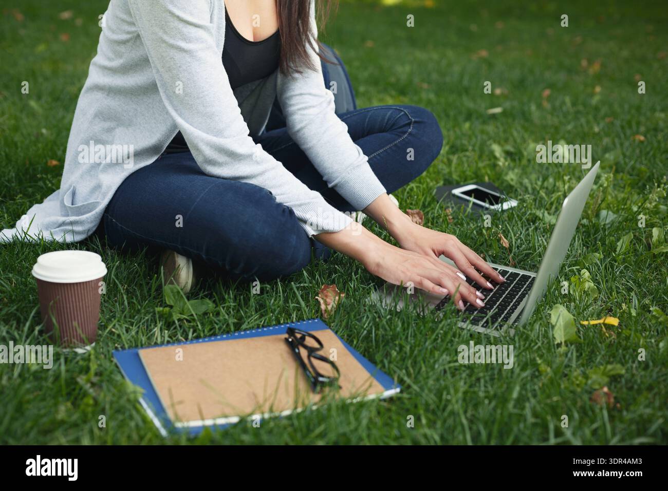 Writing on a Laptop in a Park While Enjoying Coffee and Taking Notes Stock Photo