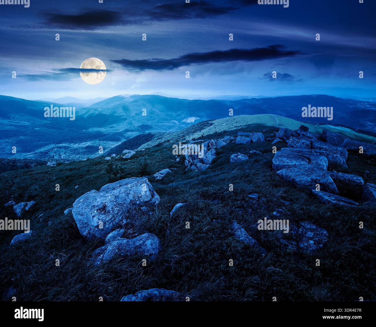 mountain landscape in summer with rocks at night. grass under dark sky in full moon light. alpine meadow and rolling hills with boulders. backdrop for Stock Photo
