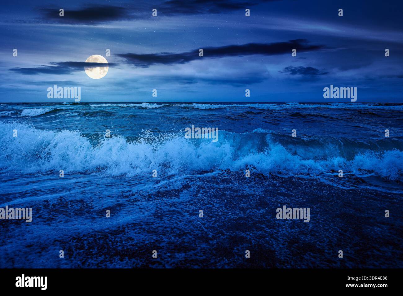 stormy weather on the sandy beach at night. dramatic sky over the sea in full moon light. moody summer landscape. waves crashing the shore. mysterious Stock Photo