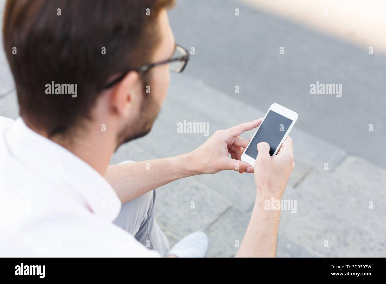 Man Using Smartphone While Sitting on Steps in an Outdoor Setting Stock Photo