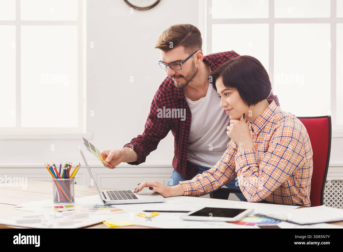 Two People Working Together in an Office on a Computer While Discussing a Project Stock Photo