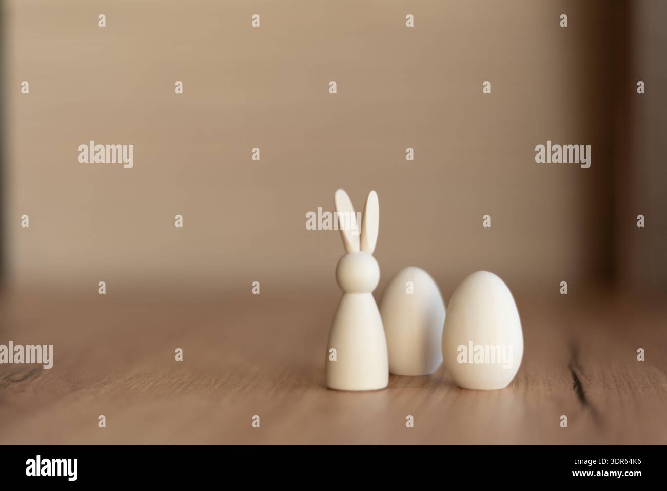 Minimal easter still life with white bunny and eggs. Minimal still life of small white wooden bunny figurine and two eggs on rustic table with soft Stock Photo
