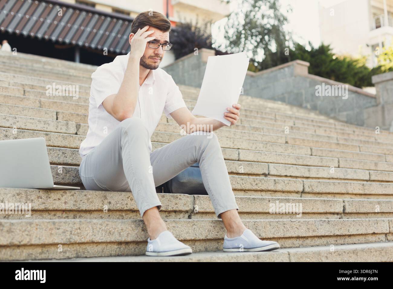 Man Reading Document While Sitting on Steps in Urban Area During Daylight Hours Stock Photo