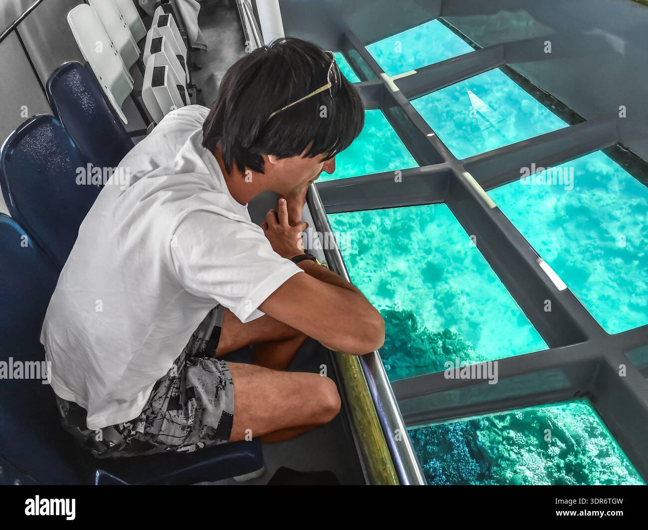 A man looks at the deep underwater life of the Red Sea through the transparent bottom of the bathyscaphe. Tourist service in Sharm El Sheikh, Egypt - Smartphone Captured Stock Image