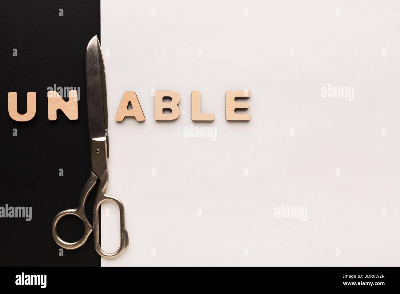 Scissors Placed Next to Wooden Letters Spelling Unable on Black and White Background Stock Photo