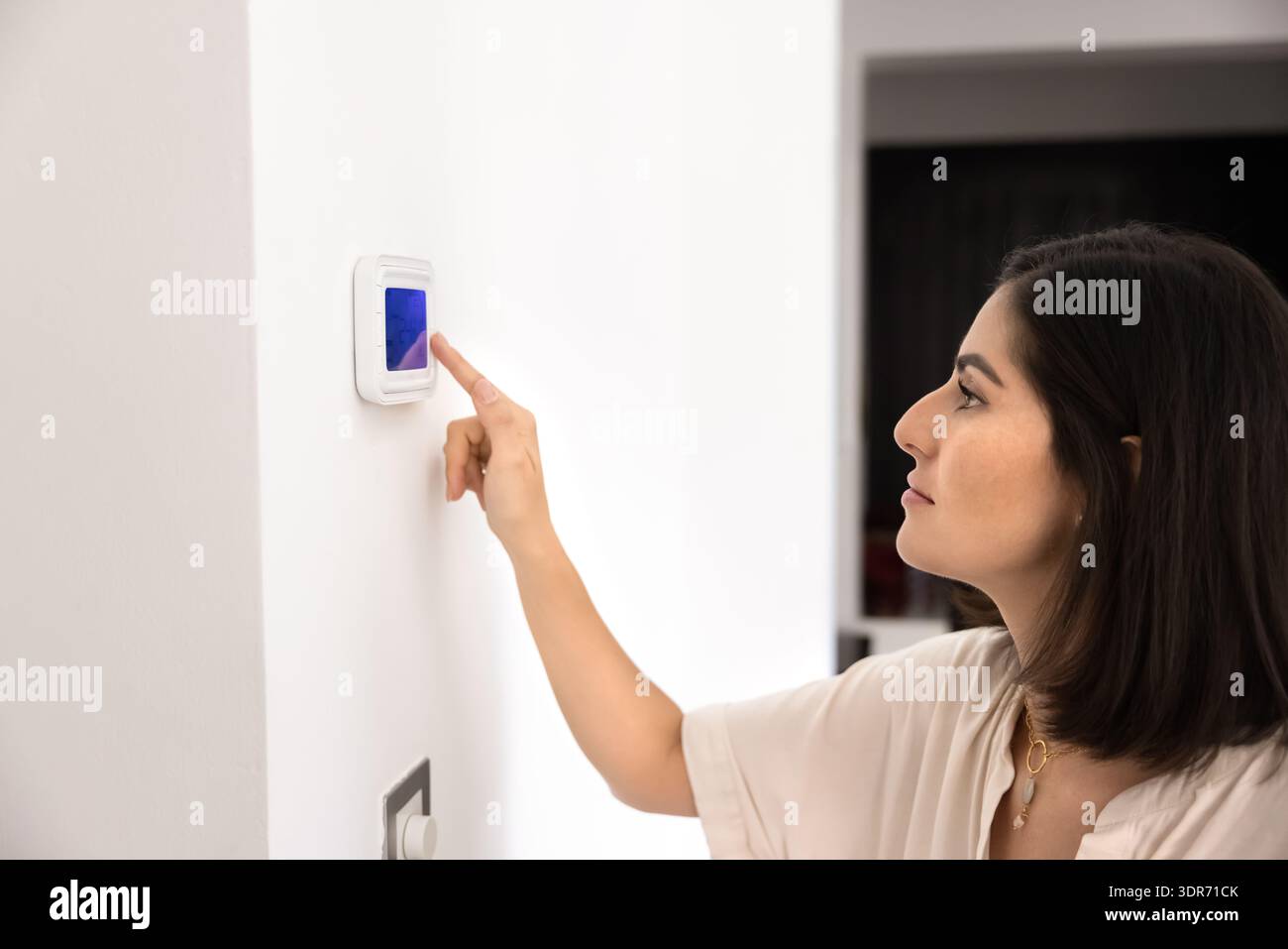 Young Hispanic woman regulating temperature on control panel indoors Stock Photo