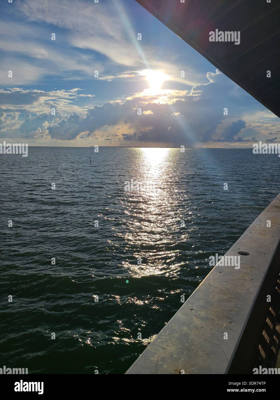 EDITORIAL USE ONLY- FT. MYERS BEACH PIER, FLORIDA:  Golden sunlight piercing through dramatic afternoon storm clouds over the Gulf of Mexico, viewed from a pier in Fort Myers, Florida. Shimmering water reflections and crepuscular rays create a peaceful coastal atmosphere during the humid Florida summer. - Smartphone Captured Stock Image