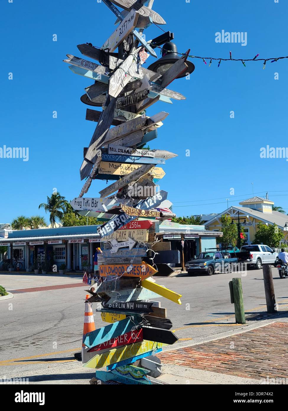 EDITORIAL USE ONLY- KEY WEST FLORIDA:  : Iconic Directional Signpost with Distances to World Cities, Key West, Florida. ​A tall, rustic wooden signpost covered in hand-painted arrows pointing toward various global destinations, including "Wildwood Crest," "Berlin NH," and "Marblehead." The sign is located in the historic seaport area under a clear blue sky. - Smartphone Captured Stock Image