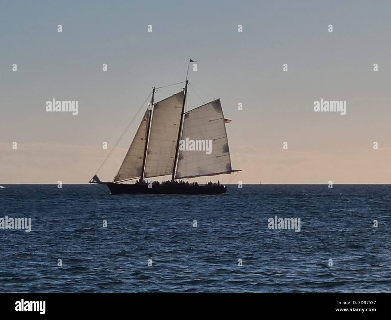 EDITORIAL USE ONLY- KEY WEST FLORIDA:  : A wide-angle view of the 105-foot Schooner America 2.0 under full sail against a clear sky in the Florida Straits. The black-hulled sailing vessel is a modern tribute to the 19th-century yacht that inspired the America's Cup. Captured during a classic sunset cruise near Key West, a popular tourist destination known for its maritime heritage. - Smartphone Captured Stock Image