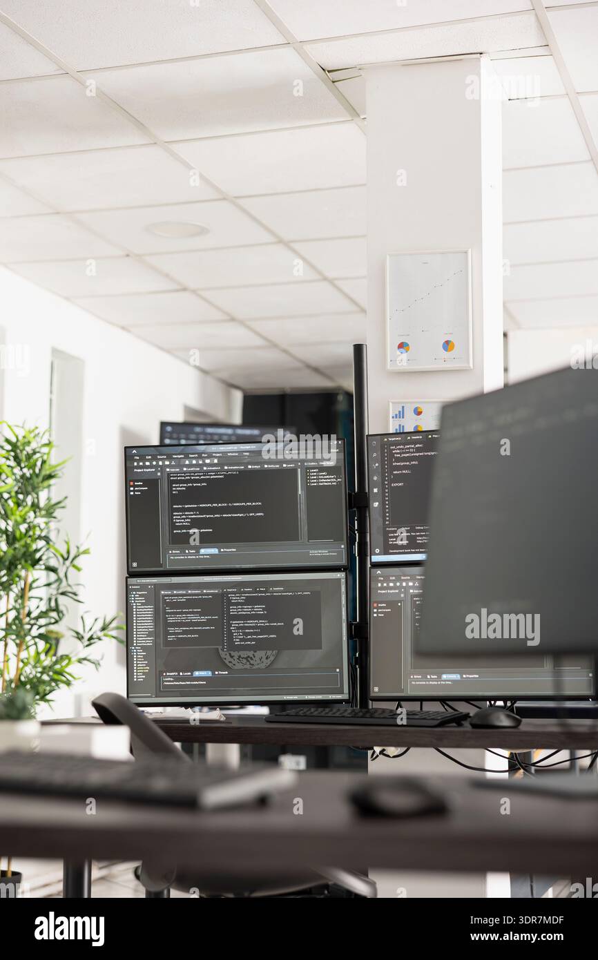 Vacant IT workspace features desk with multi monitors displaying coding scripts and system data. Empty office scene highlights innovation, software development and professional engineering workflow. Stock Photo