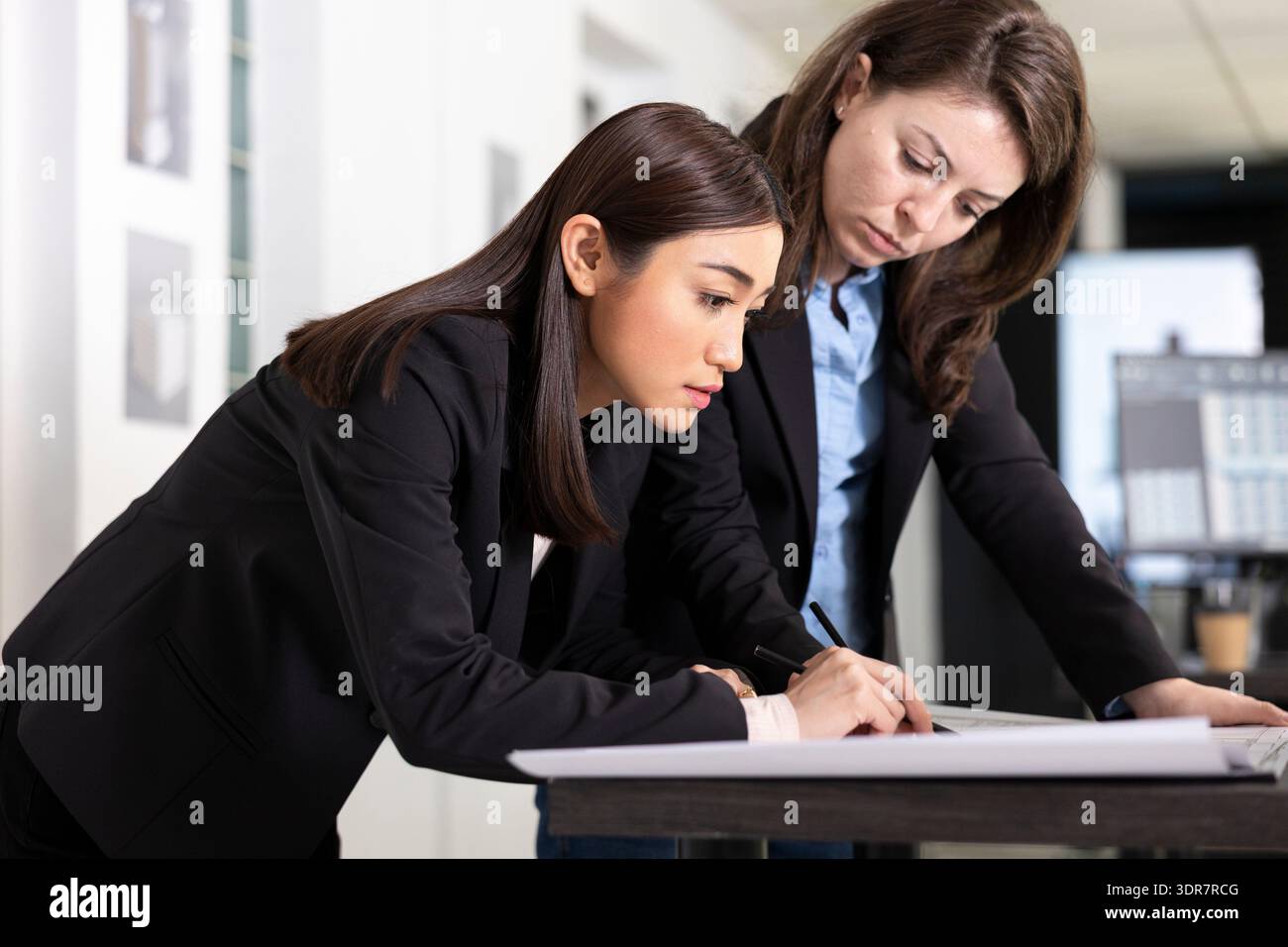 Diverse female professionals working on building designs and detailed floor plans for upcoming projects. Focused women architects collaborate closely while reviewing detailed blueprints in office. Stock Photo