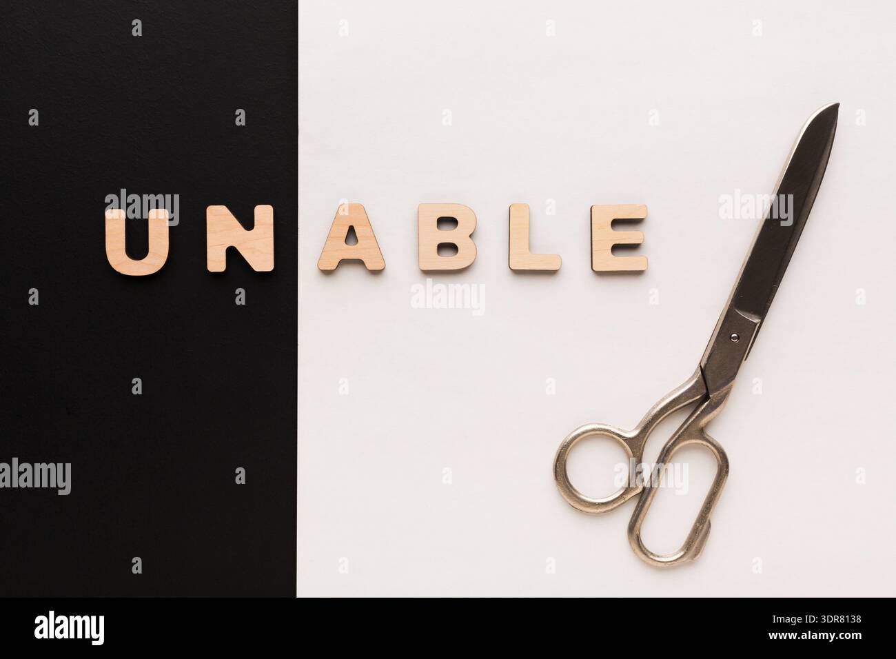 Scissors Placed Next to Wooden Letters Spelling Unable on a Contrasting Background Stock Photo