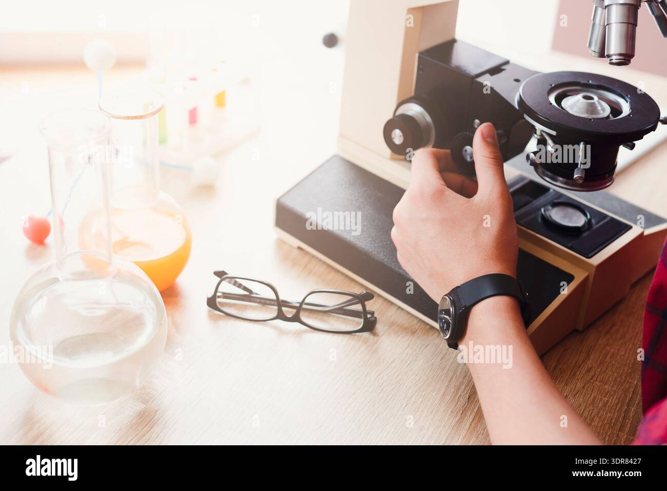 Student Conducts Experiment Using Microscope and Laboratory Equipment in a Science Classroom Stock Photo