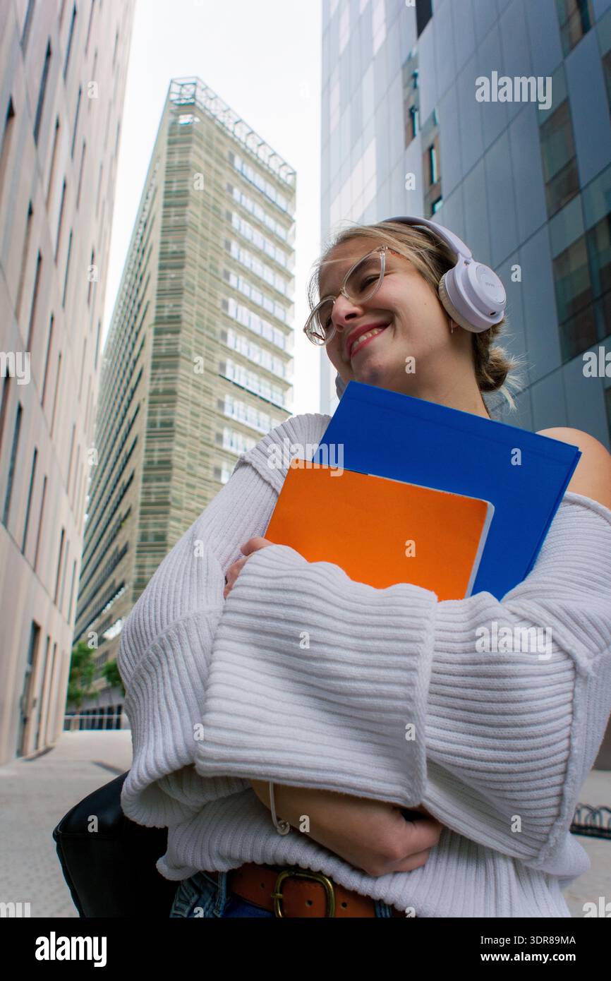 Smiling woman student walking on urban campus holding books Stock Photo