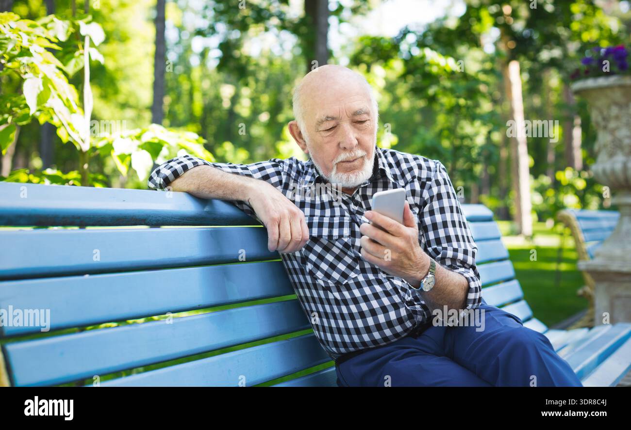 Older Man Uses Smartphone While Sitting on Bench in Park During Daytime ...