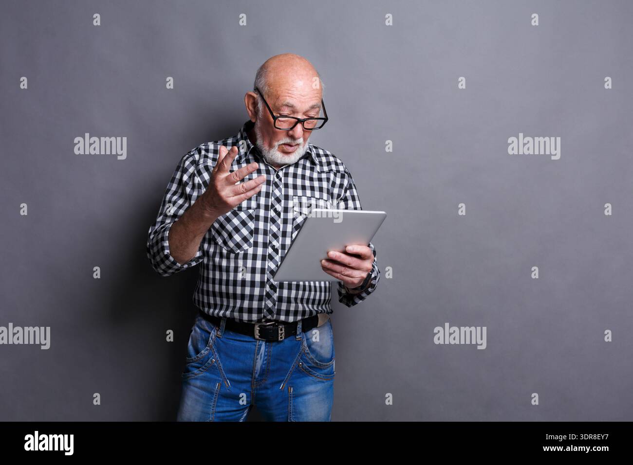Senior Man Engaged in Reading on a Tablet in a Studio With Gray Background Stock Photo