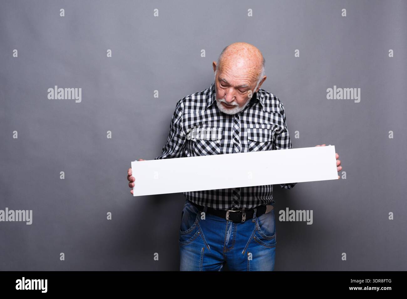 Older Man Holds Blank Sign While Looking Down in Studio With Gray Background Stock Photo