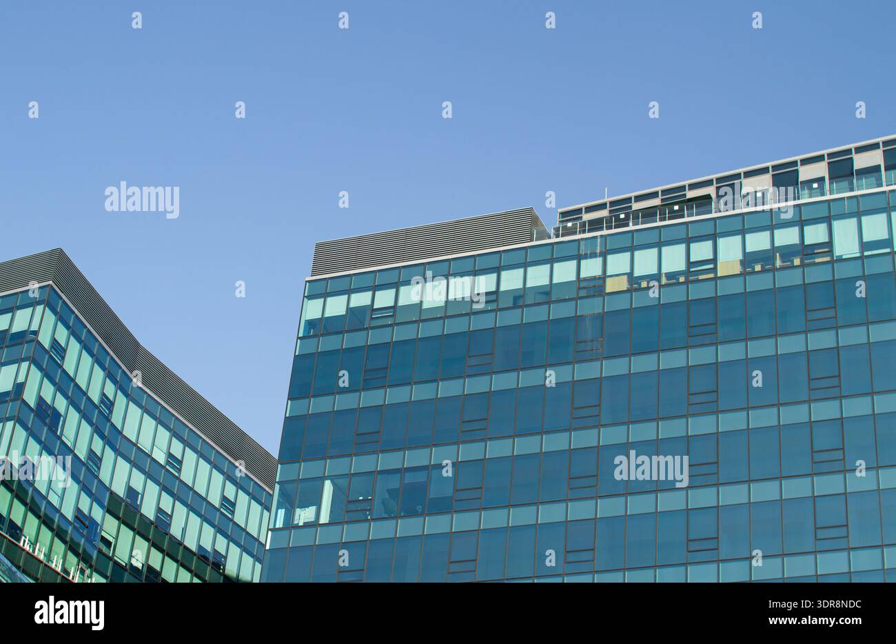 Modern glass office building with geometric facade reflecting blue sky ...