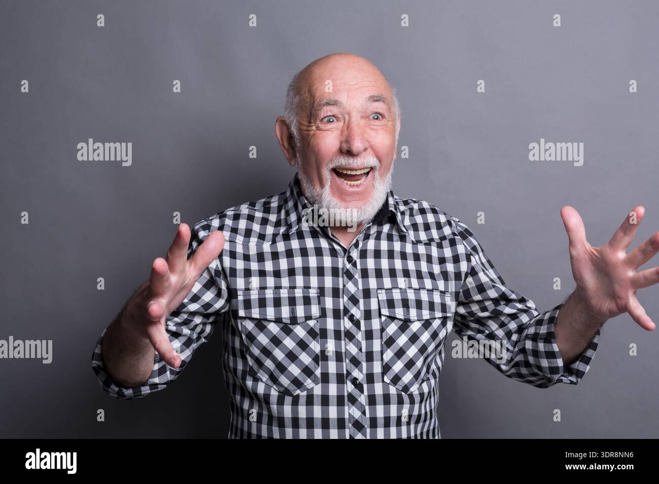 Elderly Man Smiles and Gestures With Hands Against Gray Background Stock Photo