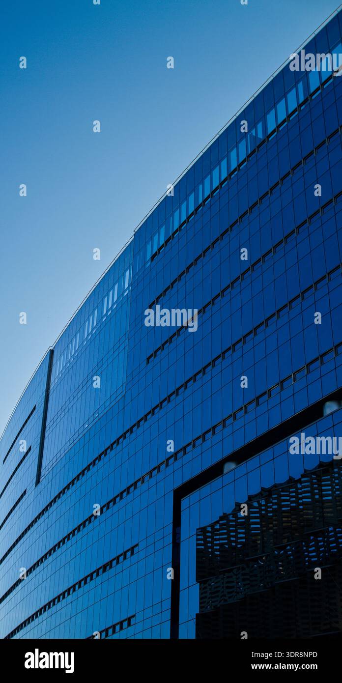 Modern glass office building with angular facade reflecting blue sky ...