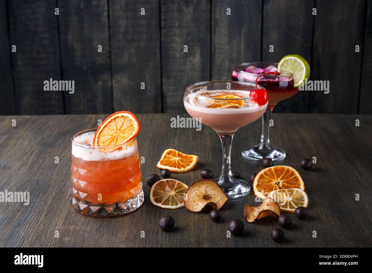 Three Colorful Cocktails Displayed on a Wooden Table With Dried Fruit Garnishes Stock Photo