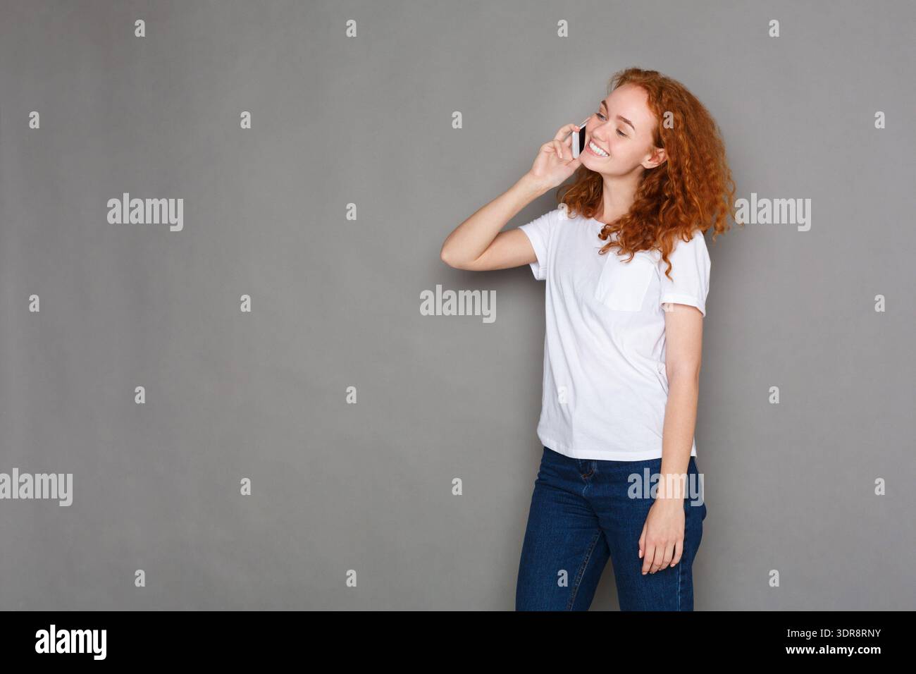 Young Woman Talking on the Phone With a Smile in a Simple Setting Stock Photo