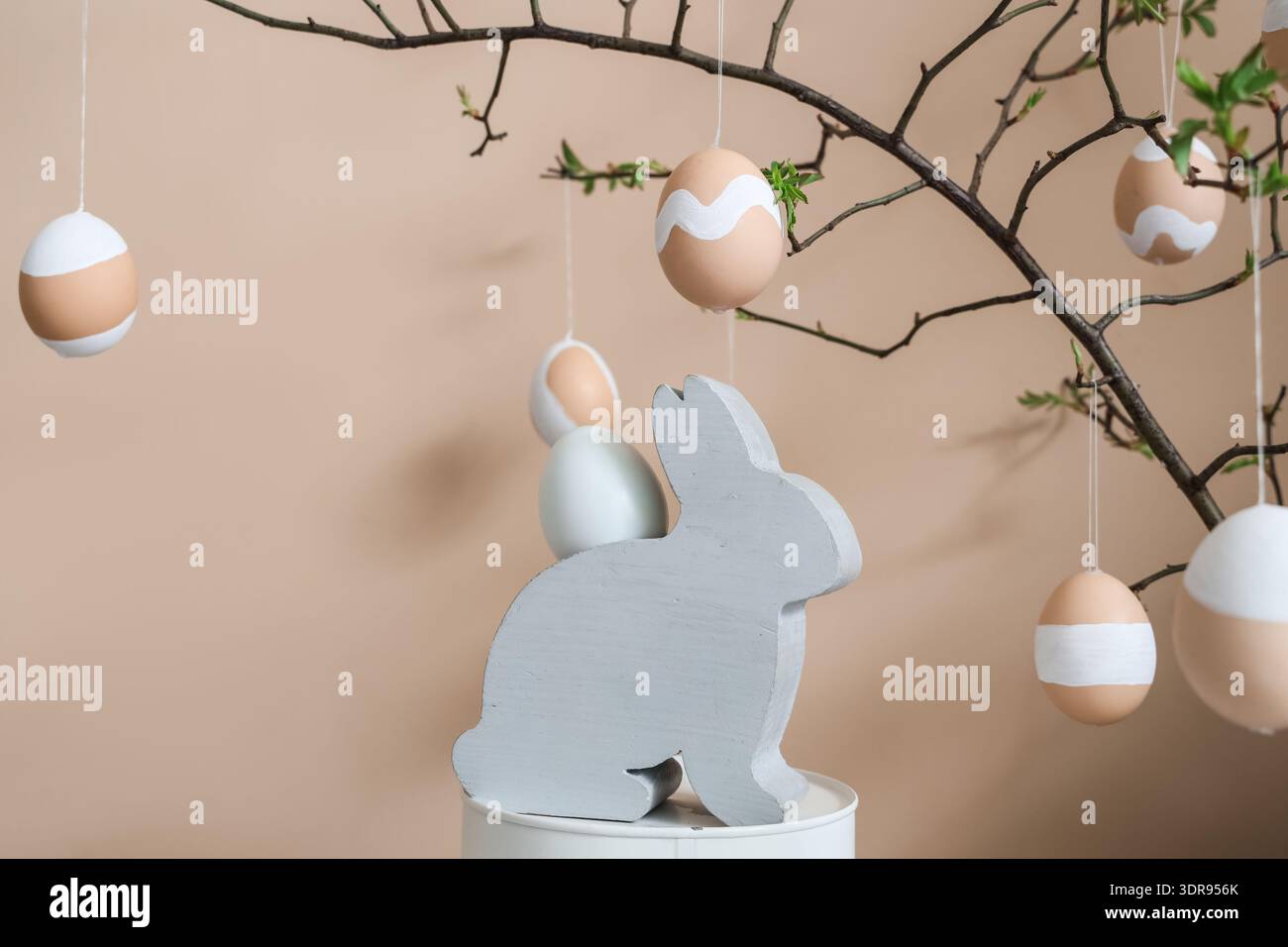 Tree branches with Easter eggs and decorative rabbit near beige wall Stock Photo