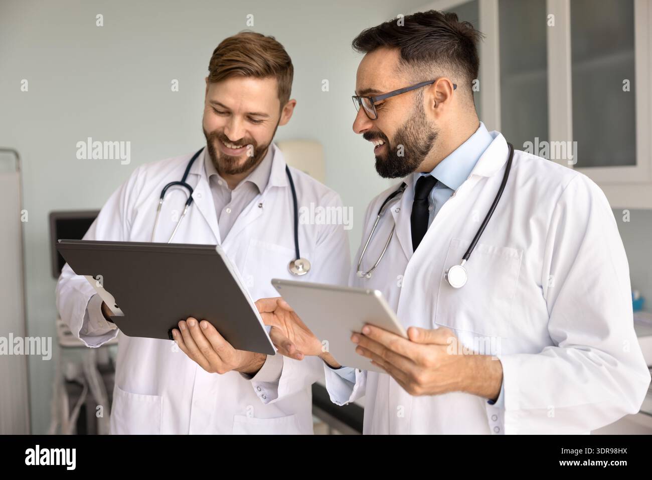 Friendly smiling male doctors discuss diagnosis using paper electronic documents Stock Photo