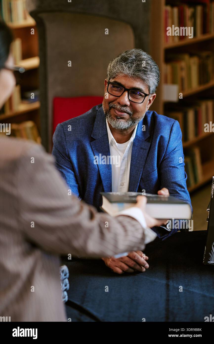 Middle Aged Man Smiling While Handing Book during Presentation Stock Photo