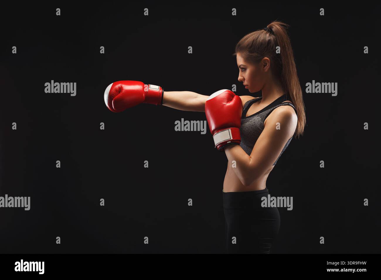 Young Woman Practices Boxing Technique With Red Gloves in Dark Setting Stock Photo