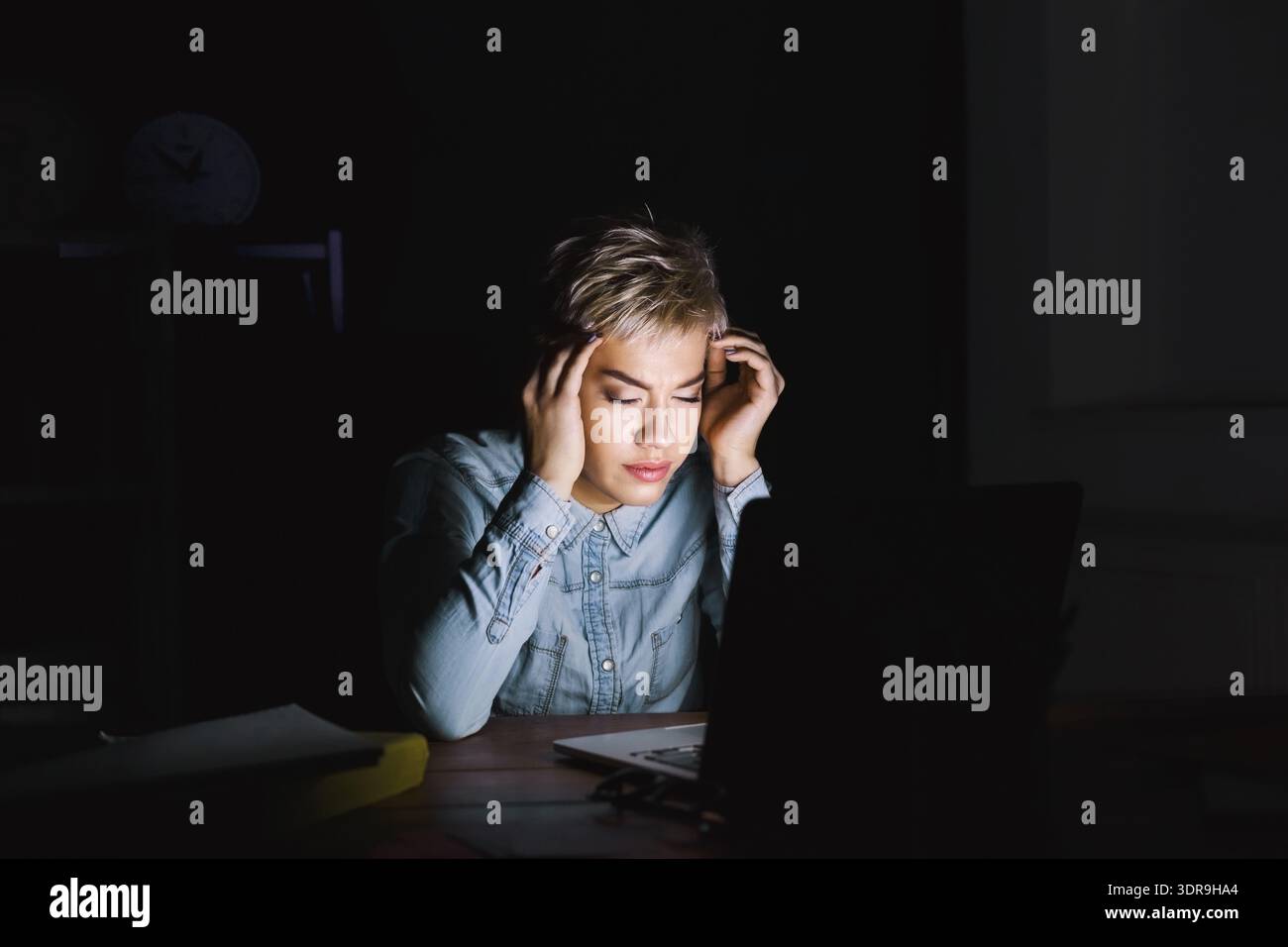 Feeling Stressed While Working on a Laptop in a Dark Room at Night Stock Photo