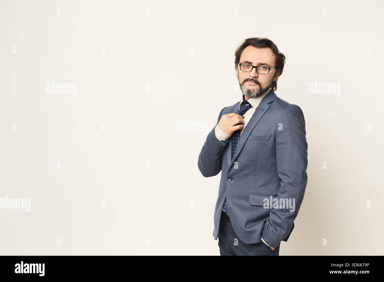 Man in Suit Adjusts Tie While Standing Against Plain Background in Studio Setting Stock Photo