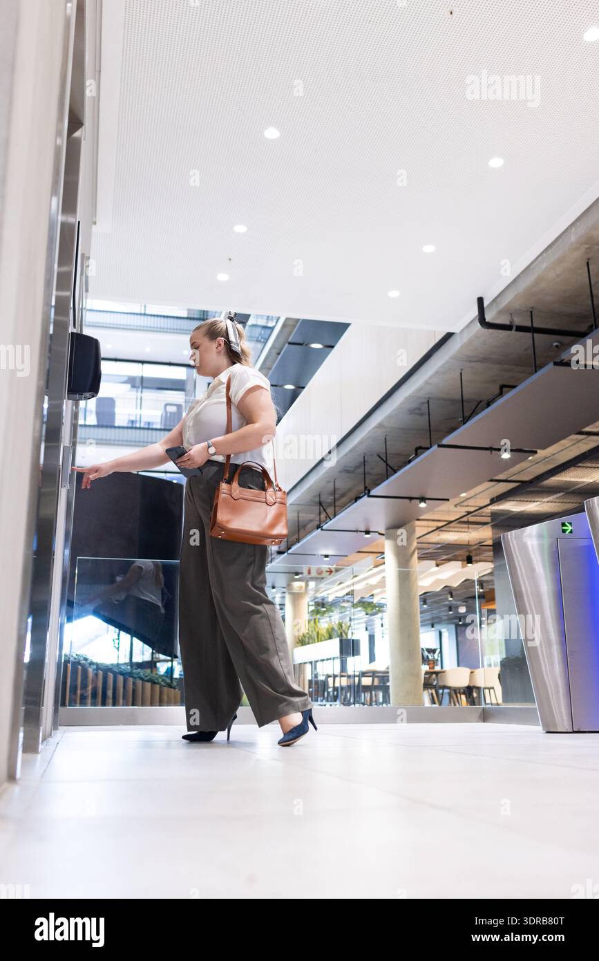 Pressing elevator button, businesswoman in office holding tablet and handbag Stock Photo