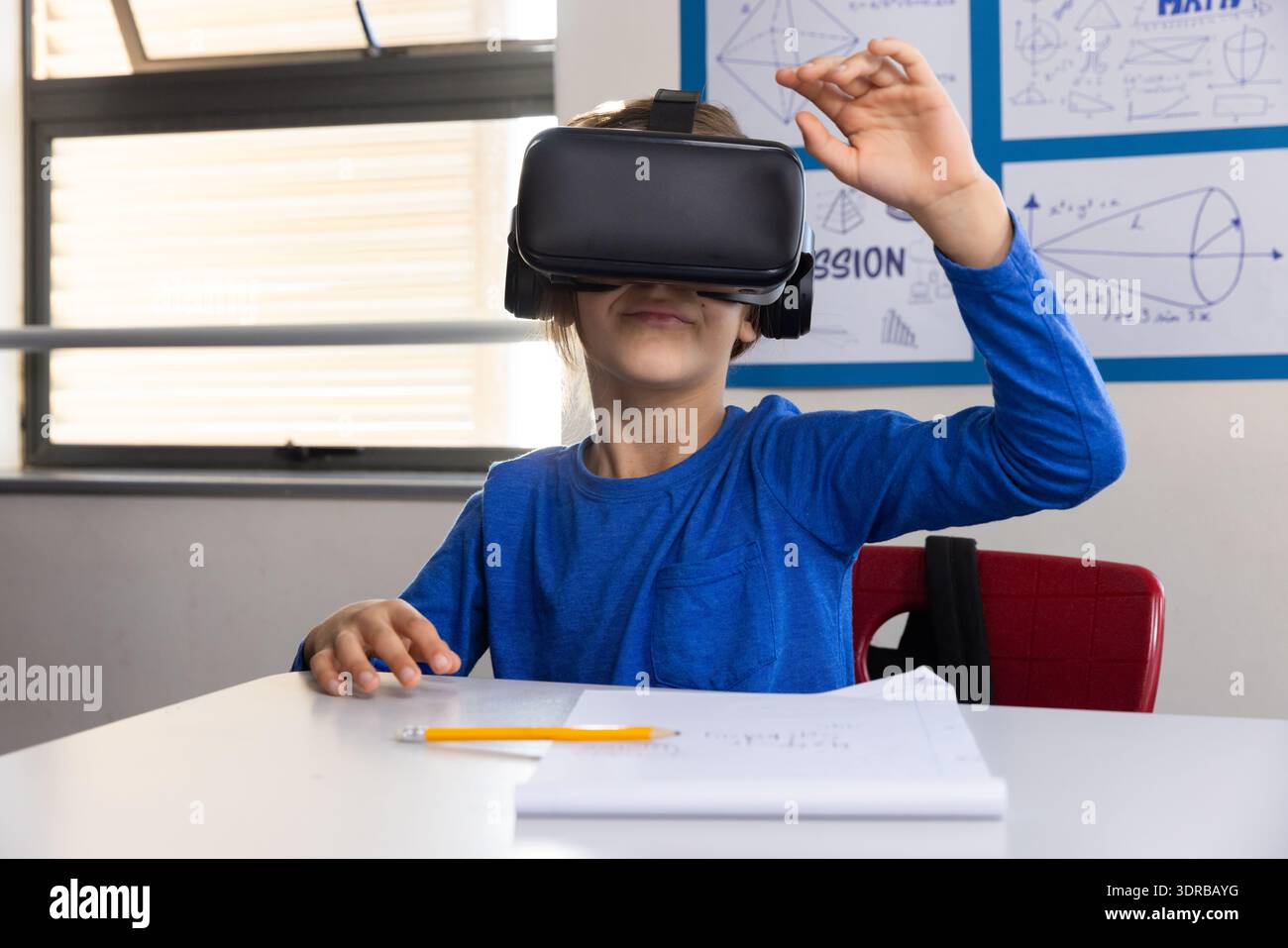 In school, boy using vr headset while sitting at desk with notebook Stock Photo