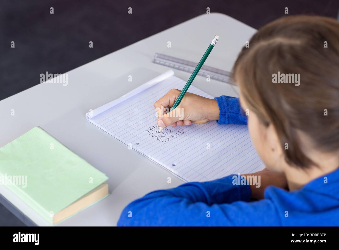 Writing math equations in notebook, boy focusing on schoolwork at desk Stock Photo