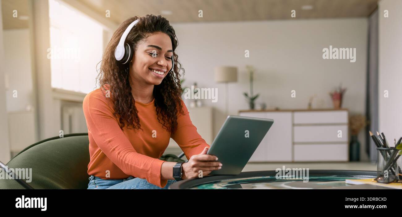 Young Woman Using Tablet at Home While Wearing Headphones During Daytime Stock Photo