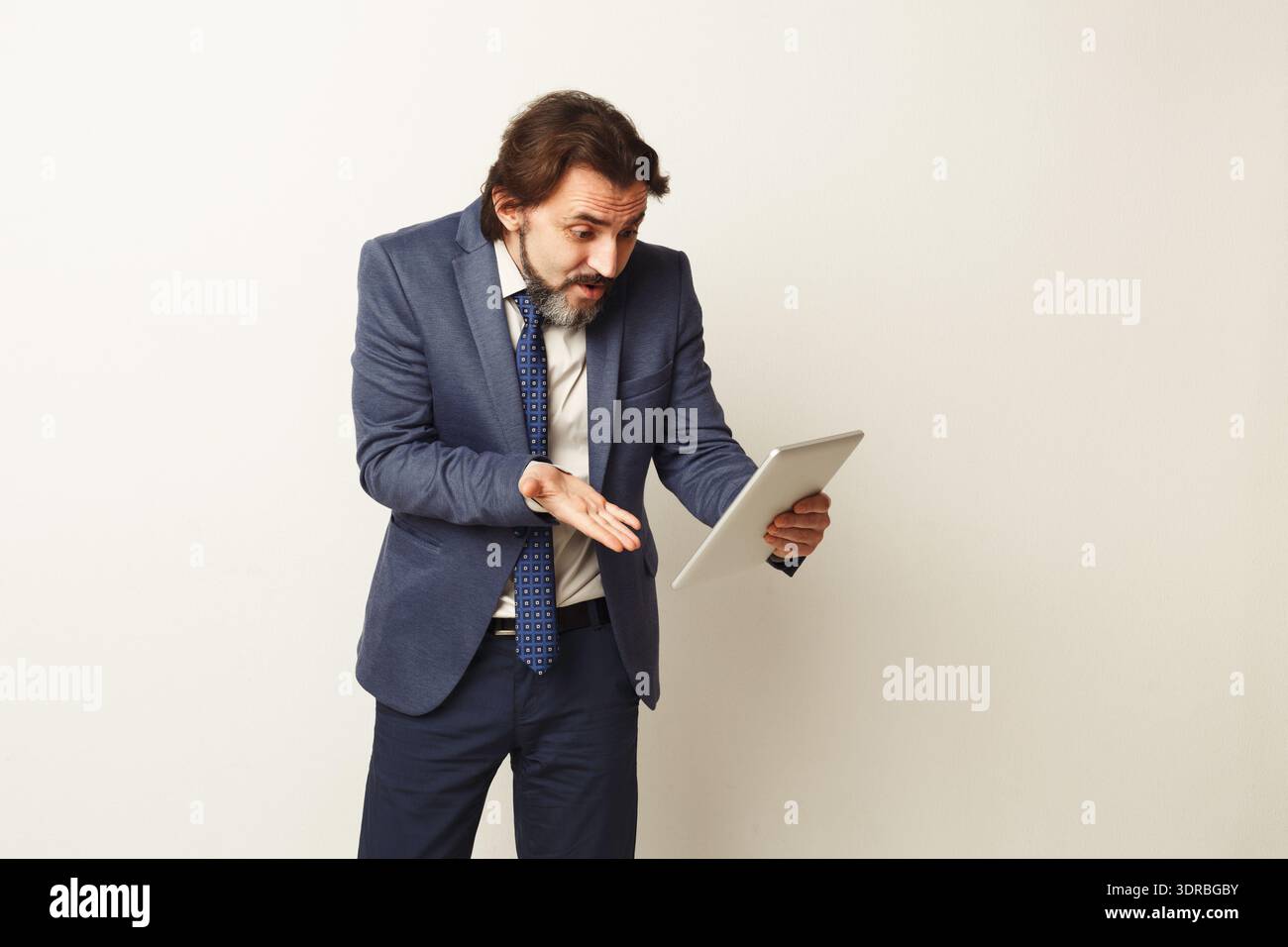 Man in Suit Looking Surprised While Holding Tablet in Office Setting Stock Photo
