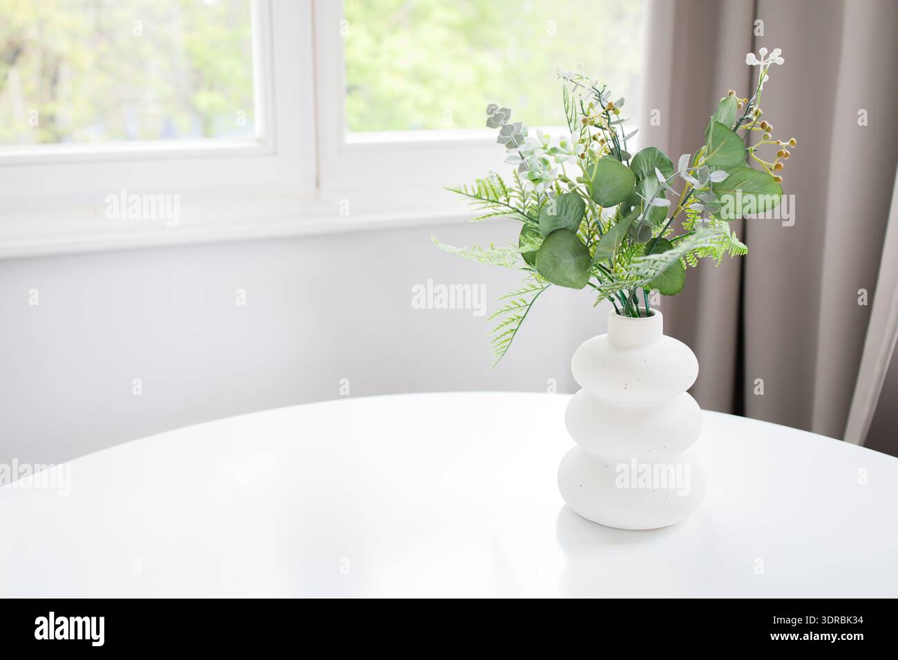 Minimalistic interior background with copy space: white table with artificial green plant in vase and window with soft morning light Stock Photo
