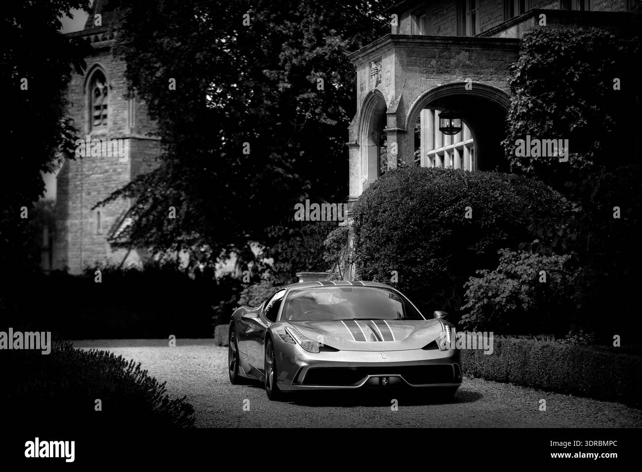Ferrari 458 speciale parked outside a historic stone house with arched entrance and lavender, photographed in a quiet English village setting. Stock Photo