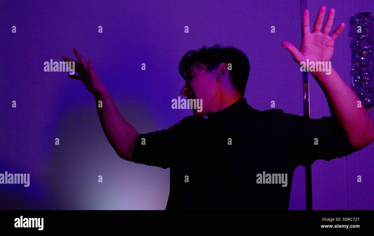 Young man dancing in a room with purple neon lighting Stock Photo