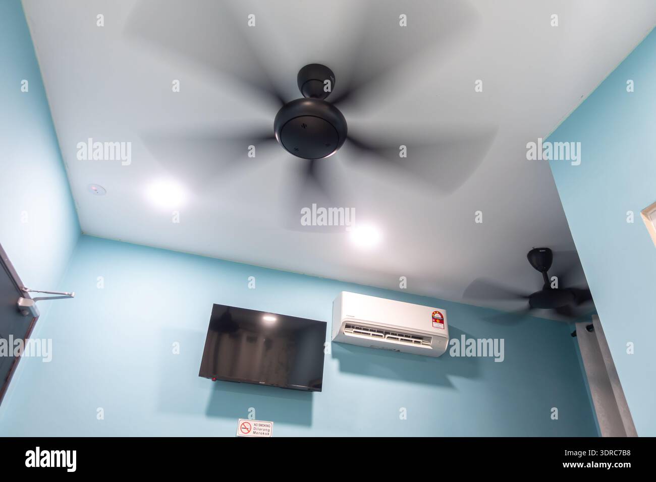 modern room interior featuring black ceiling fans and a wall-mounted air conditioner. The walls are painted in a light blue shade, flat screen tv Stock Photo