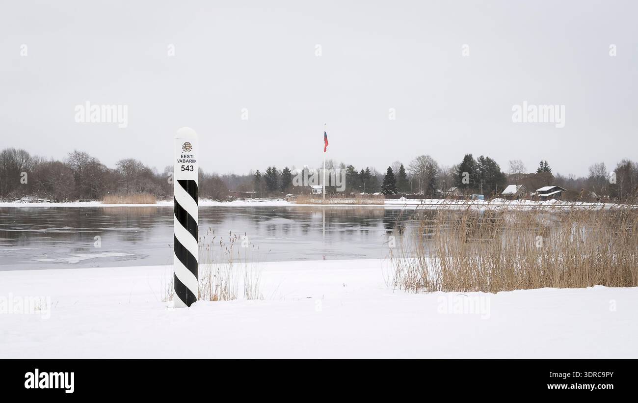 Estonian border marker number 543 stands along a frozen river in Vasknarva during a quiet winter day. Snow-covered riverbank at the Estonia border. Stock Photo