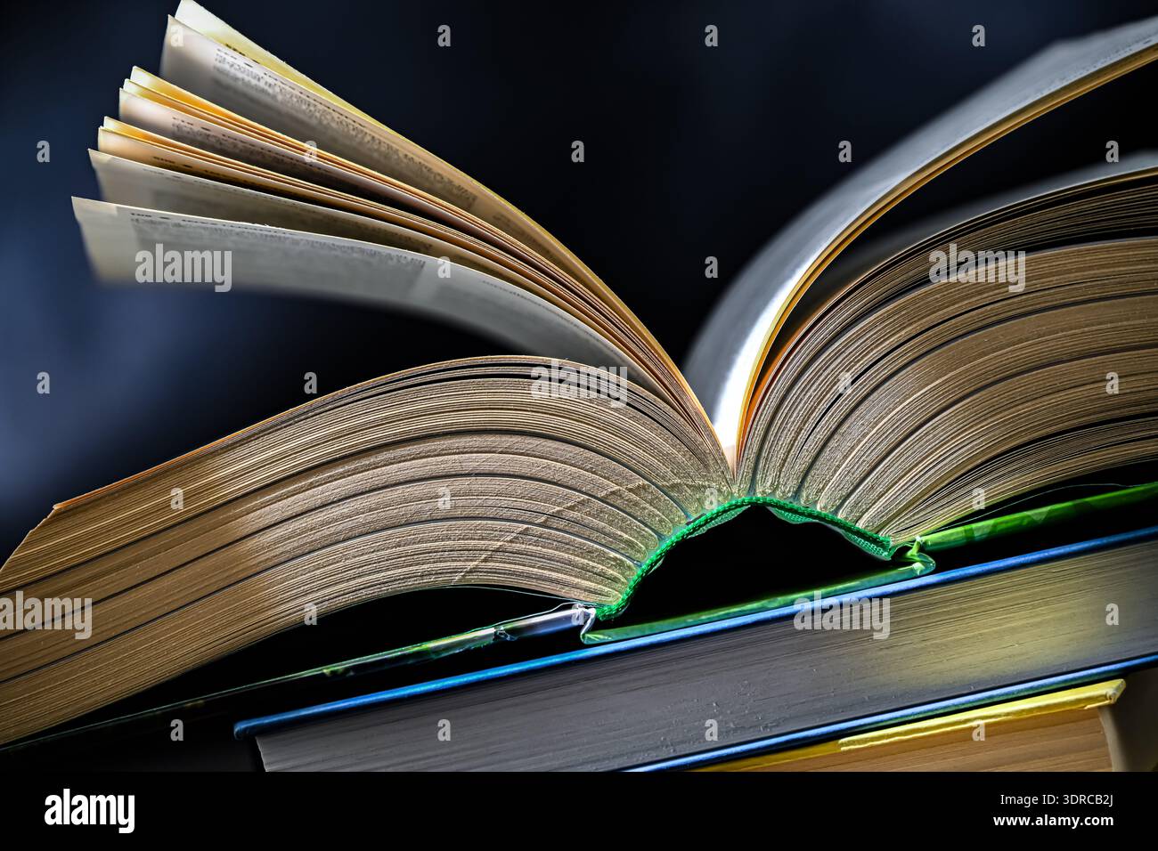 An open book lying on a stack of other books. Stock Photo
