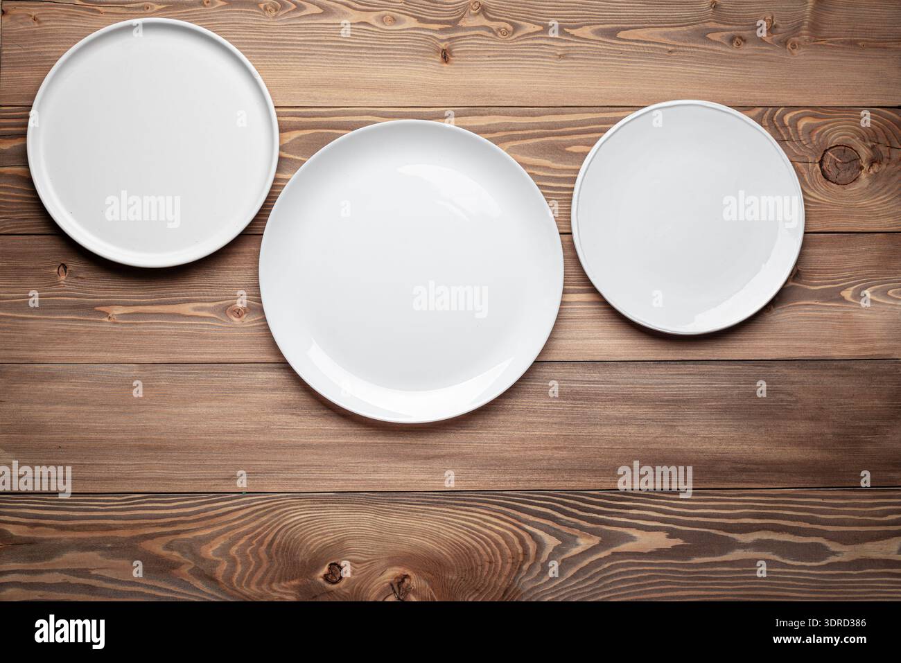 Three empty white plates on wooden table background Stock Photo